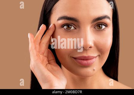 Bella bella bruna donna millenaria che tocca rughe vicino ai templi, primo piano Foto Stock
