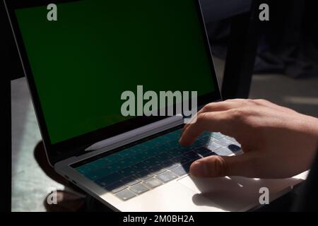 Un uomo che utilizza un computer portatile con uno schermo verde colorato. La luce del sole cade sulla tastiera del notebook. Con spazio per copiare. Foto di alta qualità Foto Stock