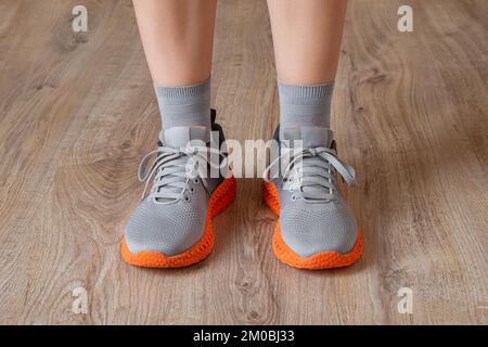 Sneaker grigie e calze grigie sui piedi della donna. I piedi in piedi si sfoggiano in sneaker in mesh con suola arancione scanalata. Nuove scarpe per uno stile di vita attivo. Foto Stock