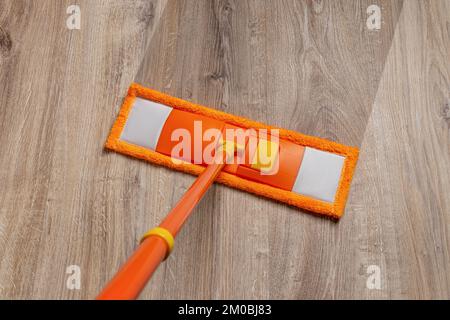 Spazzolone arancione lavaggio pavimento polveroso a casa. Pulire il pavimento in legno laminato con un mocio in microfibra umido. Pulizia del pavimento. Pulizia e routine dei compiti. Foto Stock