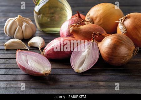 Scalogno rosso fresco, cipolla gialla e aglio su fondo di legno nero. Closeup di eschalots lunghi interi e dimezzati. Bulbi di cipolla e spicchi d'aglio. Foto Stock