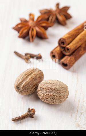 Semi interi di noce moscata, pochi chiodi di garofano, anice stellato e bastoncini di cannella su fondo di legno bianco. Spezie per autunno zucca torta macro. Cucinare piatti autunnali Foto Stock