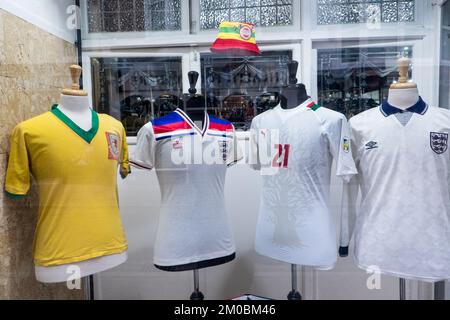 Raro,autentico,football,camicie,non,fan,replica,football shirts,on,display,durante,Qatar,Coppa del mondo,Coppa del mondo,Inverno,2022,in,negozio,vetrina,at,Clive,Continental menswear,negozio,Terrace Road,Aberystwyth,Town,center,West,Wales,GB,Gran Bretagna,Gran Bretagna,Regno Unito,Gran Bretagna,Regno Unito,Gran Bretagna,Regno Unito,Gran Bretagna. Il display,prestato,da,calcio,collezionista,include,due magliette inglesi,a,camicia gallese gialla,e,a,Senegal,camicia,e,calcio,stivali,indossati,e,firmati,da,gallese,calcio,leggenda,Gareth Bale. La camicia gialla è una camicia del Galles indossata di corrispondenza, indossata, AT, World Cup.classic 1958, Inghilterra 1981, camicia, numero 7, indossata, da Kevin Keegan. Foto Stock