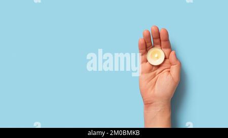 Candela da tè nella mano palma su sfondo blu. Candela rotonda profumata che brucia in una donna caucasica mano destra. Candele per il concetto di aromaterapia Foto Stock