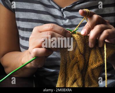 Donna in maglia, in abito a righe. Primo piano della lavorazione a maglia delle mani. Foto Stock