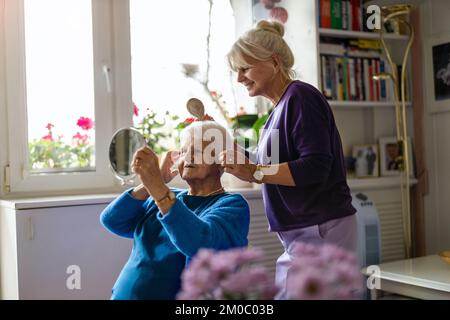 Donna che pettina i capelli di madre anziana Foto Stock