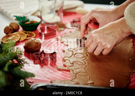 Le mani femminili tagliano le figure dalla pasta dello zenzero con il taglierino. Cucinare biscotti di pan di zenzero per prepararsi per le vacanze invernali. Cottura di Natale Foto Stock