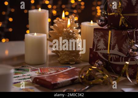 scatole con confezione fotografica e regali in piedi su un tavolo con candele accese sullo sfondo appeso ghirlanda festiva Foto Stock