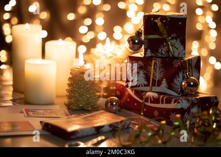 Foto presenti stand in una fila verticale avvolto in carta festiva sono sul tavolo accanto a candele accese, sullo sfondo un bokeh di Natale festivo l Foto Stock