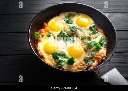 Padella di uova fritte e pomodori su una superficie scura del tavolo, vista dall'alto. Colazione con uova. Uova per colazione Foto Stock