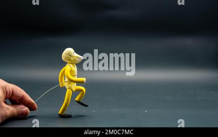 Processo di stopmotion di camminare. Quarta fase. Mano dell'uomo che tiene con un filo di alluminio una figura fatta con pasta modellante gialla che comincia il processo di Foto Stock