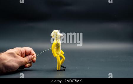 Processo di stopmotion di camminare. Secondo passo. Mano dell'uomo che tiene con un filo di alluminio una figura fatta con pasta modellante gialla che comincia il processo di Foto Stock