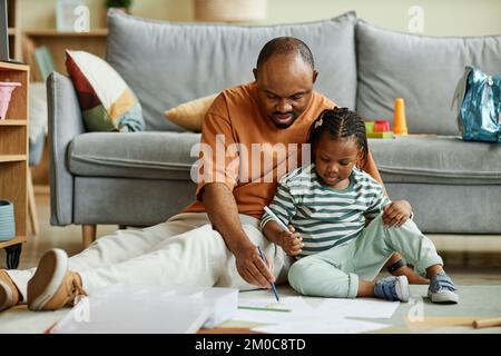 Ritratto completo di disegno nero di padre di cura immagini con ragazza carina mentre seduto sul pavimento a casa Foto Stock
