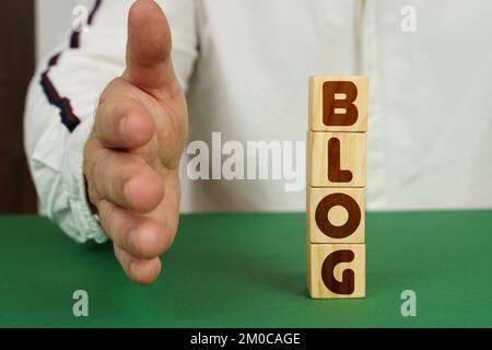 Concetto aziendale. Su una superficie verde, cubi con l'iscrizione - Blog. L'uomo tiene la mano. Foto Stock