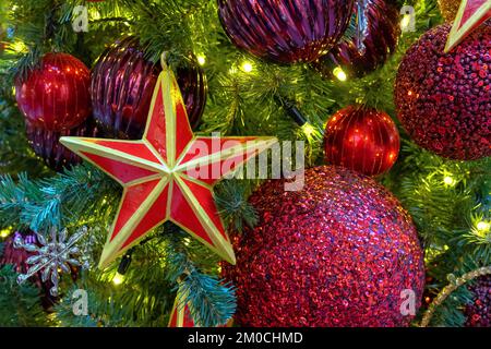 Stella rossa a cinque punte con un bordo dorato sull'albero di Natale con ghirlande. Foto Stock