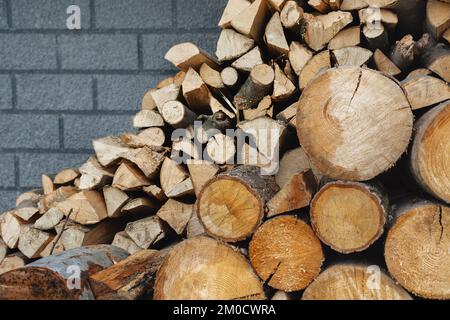 Preparazione del legno per l'inverno. Pila di legna da ardere di fronte al muro di mattoni della casa. Tronchi e tronchetti. fonti alternative di calore Foto Stock