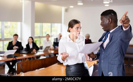 Boss di sesso maschile africano di mezza età che licenziano una giovane lavoratrice di brunette bianche Foto Stock