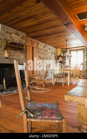 Antico tavolo da pranzo e sedie arrotondate con schienale alto nella sala da pranzo con pavimento in legno all'interno di una vecchia casa in pietra di campo in stile cottage canadese del 1722. Foto Stock