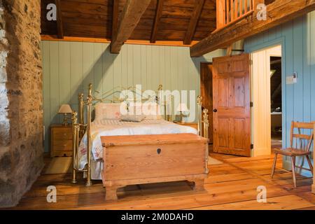 Cassettiera anticata e letto in ottone nella camera da letto principale al piano superiore all'interno di una vecchia casa in pietra di campo in stile cottage Canadiana del 1722. Foto Stock