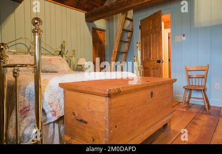 Cassettiera anticata e letto in ottone nella camera da letto principale al piano superiore all'interno di una vecchia casa in pietra di campo in stile cottage Canadiana del 1722. Foto Stock