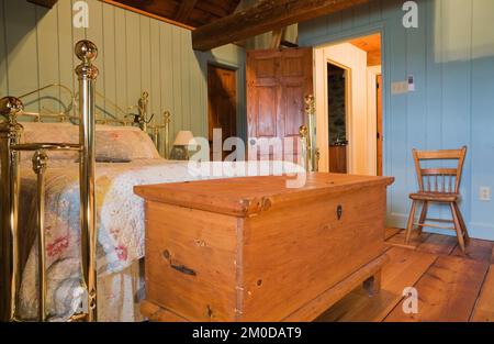 Cassettiera anticata e letto in ottone nella camera da letto principale al piano superiore all'interno di una vecchia casa in pietra di campo in stile cottage Canadiana del 1722. Foto Stock