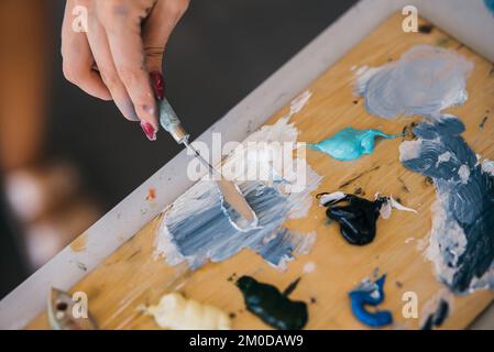 Primo piano delle pitture della miscela della mano della donna nella tavolozza Foto Stock