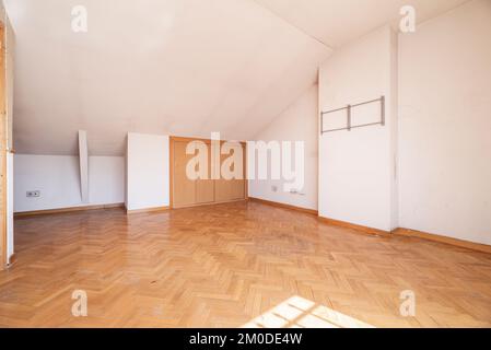 Soggiorno vuoto mansardato e armadi con porte scorrevoli in legno nell'ala, pavimenti in parquet di quercia francese Foto Stock