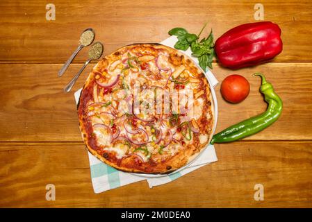 Grande pizza italiana in crosta sottile con cipolle rosse, pollo fritto, spezie, peperoni verdi e rossi e un pomodoro Foto Stock