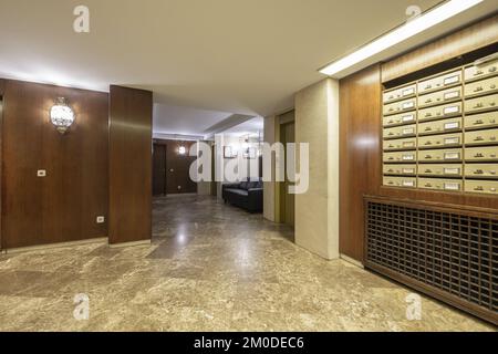 Portale di un edificio residenziale con pareti rivestite in legno, cassette postali in ottone, divani di cortesia e diversi ascensori Foto Stock