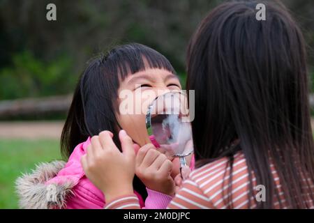 Due sorelle felici esplorano la natura con lente d'ingrandimento all'aperto. Bambino che gioca nella foresta con lente d'ingrandimento. Concetto di educazione e scoperta. Foto Stock