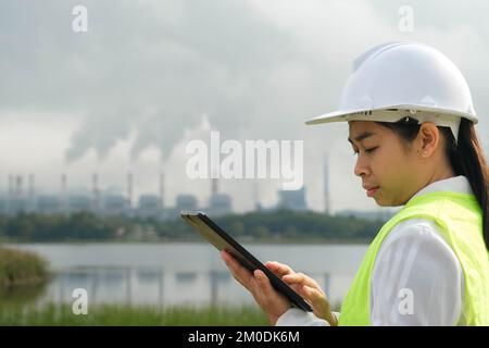 Capo ingegnere donna che indossa un giubbotto verde e il casco si trova all'esterno sullo sfondo della centrale a carbone e vapore nella nebbia mattutina. Foto Stock