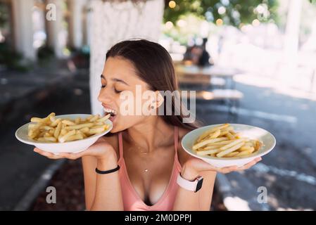 Le giovani donne tengono patatine fritte su piatti bianchi. Street cafe Foto Stock