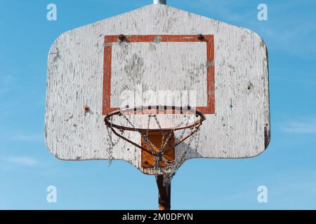 Primo piano di un vecchio backboard da basket in legno e cerchio rosso con sfondo cielo blu Foto Stock