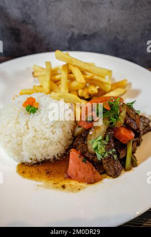 lomo saltado con riso bianco e patatine fritte, servito su tavola di legno Foto Stock