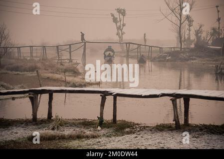 Srinagar, India. 05th Dec, 2022. Un uomo cammina lungo un ponte di legno mentre gli uomini ranghi le loro barche durante una fredda mattina all'interno del lago dal. La temperatura minima continua a stabilizzarsi al di sotto del punto di congelamento nella valle, poiché la maggior parte delle stazioni registrava una temperatura inferiore allo zero. Srinagar, la capitale estiva di Jammu e Kashmir, ha registrato la notte più fredda della stagione a meno 3,4 gradi Celsius oggi. (Foto di Idrees Abbas/SOPA Images/Sipa USA) Credit: Sipa USA/Alamy Live News Foto Stock