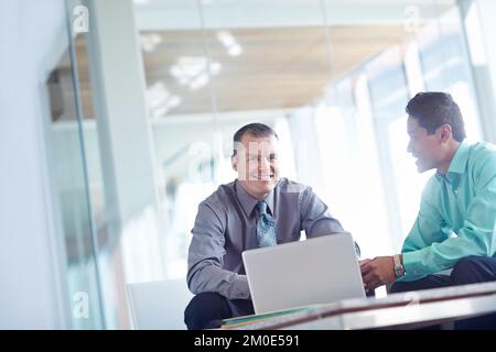 Lavorano bene come una squadra. Due bei giovani uomini d'affari che lavorano insieme mentre condividono un notebook tra loro. Foto Stock