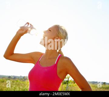 L'idratazione è importante di fronte a un rigoroso esercizio. Una bella giovane donna in abbigliamento sportivo bere acqua da una bottiglia. Foto Stock