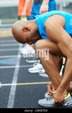 Ottenere loro bello e stretto per la corsa. Vista laterale di un atleta maschile che legava le scarpe in preparazione alla gara. Foto Stock