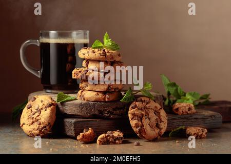 Biscotti al cioccolato appena sfornati con menta e una tazza di caffè nero su uno sfondo marrone rustico. Foto Stock