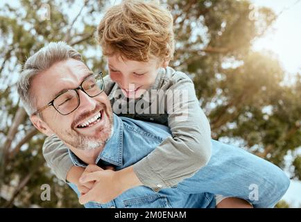 Felice padre caucasico che porta divertente figlio piccolo sulla schiena per un giro a piggyback in giardino o cortile esterno. Sorridente genitore legame con adorabile Foto Stock