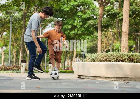 Padre e figlio giocano a calcio nel parco il sabato mattina Foto Stock