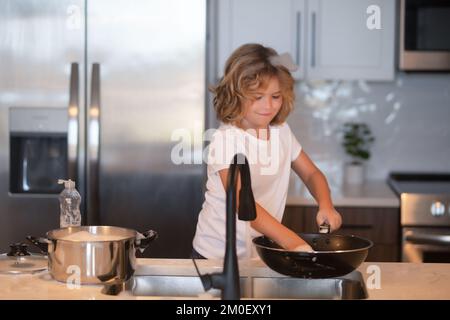 Stoviglie per bambini con spugna. Pulizia dei materiali di consumo. Contribuire alla pulizia. Obblighi di pulizia. Piatti di lavaggio per bambini. Bambino ragazzo lavare piatti in cucina Foto Stock