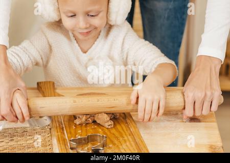 le mani della ragazza tirano fuori l'impasto dello zenzero con un mattarello nella cucina. Ragazza che prepara i biscotti di natale su un tavolo di legno Foto Stock