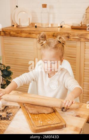 le mani della ragazza tirano fuori l'impasto dello zenzero con un mattarello nella cucina. Ragazza che prepara i biscotti di natale su un tavolo di legno Foto Stock