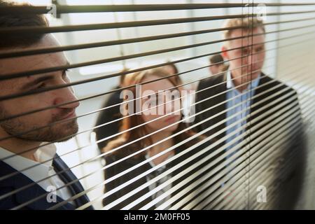 attraverso i colleghi blinds.young di affari che guardano attraverso la finestra dell'ufficio. Foto Stock