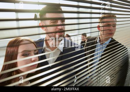 attraverso i colleghi blinds.young di affari che guardano attraverso la finestra dell'ufficio. Foto Stock