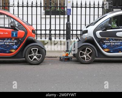 Due auto elettriche intelligenti Renault Twizys che si caricano con una prolunga elettrica collegata a una casa in una strada a Londra, carica EV, EV manuale Foto Stock