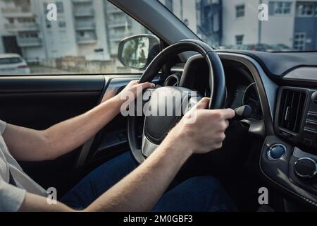 L'uomo che guida la sua nuova auto si trova davanti al volante, in primo piano il conducente fiducioso sulle strade della città Foto Stock