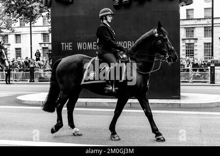 Un ufficiale di polizia femminile montato passa accanto al Monumento delle Donne della seconda guerra mondiale a Whitehall, Londra, Regno Unito. Foto Stock