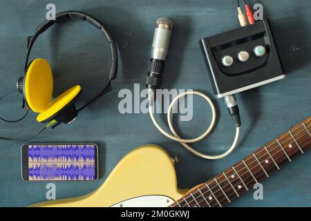 Concetto di musica o podcast con cuffie eleganti, microfono vintage, smartphone, interfaccia audio e chitarra su tavolo blu, vista dall'alto, piatto Foto Stock